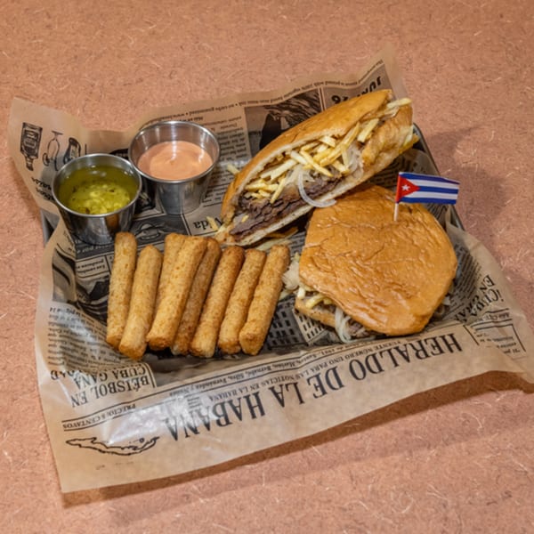 Cuban Diner's Cuban sandwich with fries, sauces, and a Cuban flag on newspaper-lined tray.