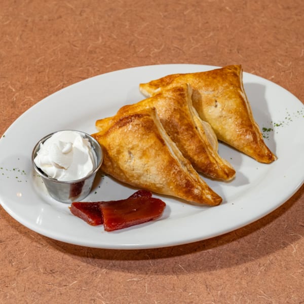 Three golden-brown Cuban pastries, guava paste, and whipped cream on a white plate.