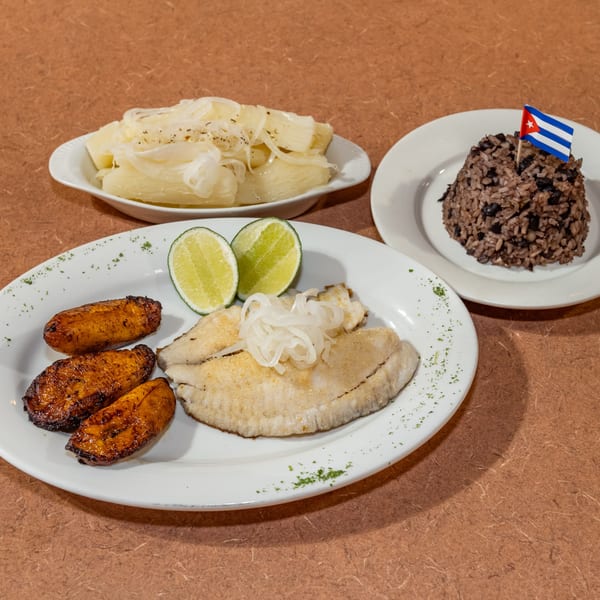Cuban meal with fried fish, plantains, lime, yucca with onions, and rice with beans.