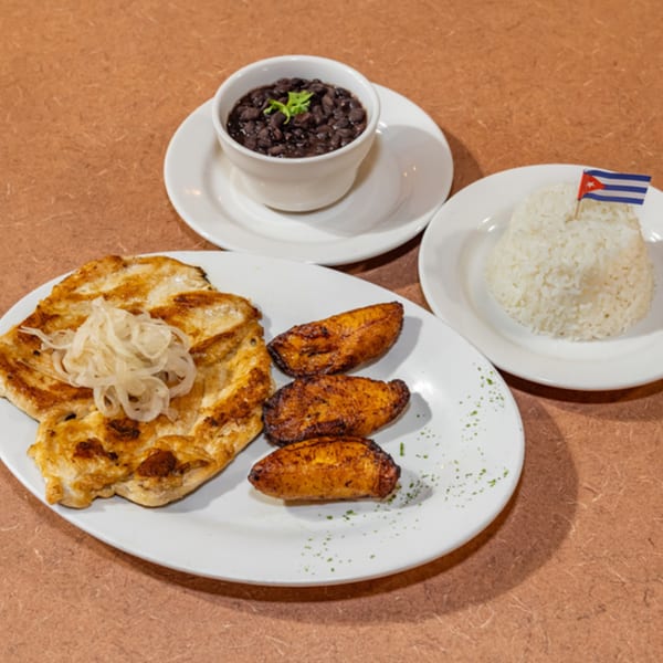 Cuban Diner's grilled chicken with onions, fried plantains, black beans, and white rice with a Cuban flag.
