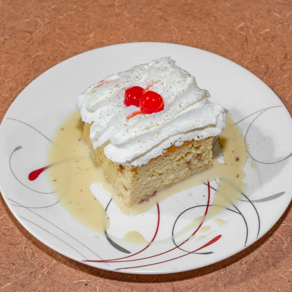A slice of Cuban tres leches cake with whipped cream, two cherries, and a creamy sauce.