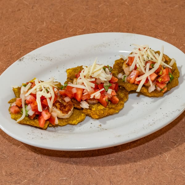 Three Cuban tostones topped with shrimp, diced tomatoes, onions, and shredded cheese on a white plate.