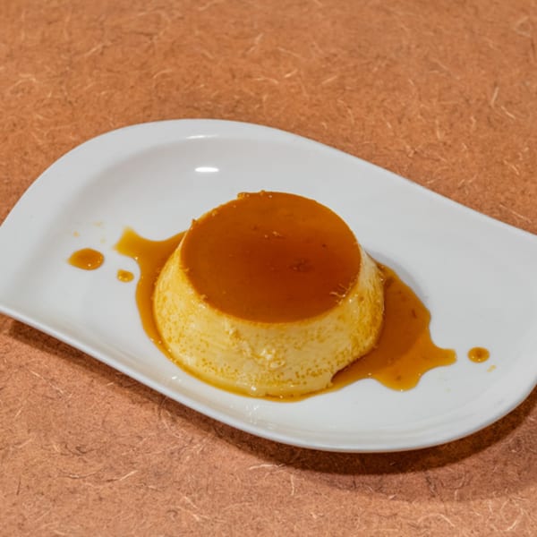 A Cuban flan dessert, a creamy custard with a rich caramel topping, on a white plate.