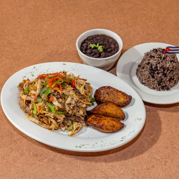 Cuban shredded chicken with peppers, fried plantains, black beans, and rice with a Cuban flag.